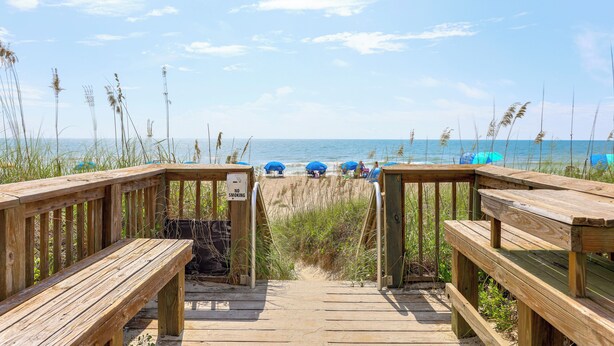 A wooden boardwalk leading to a beach with blue umbrellas and a 'No Smoking' sign. - Carolina Beach Condo w/ Marina View, on Boardwalk (Carolina Beach)