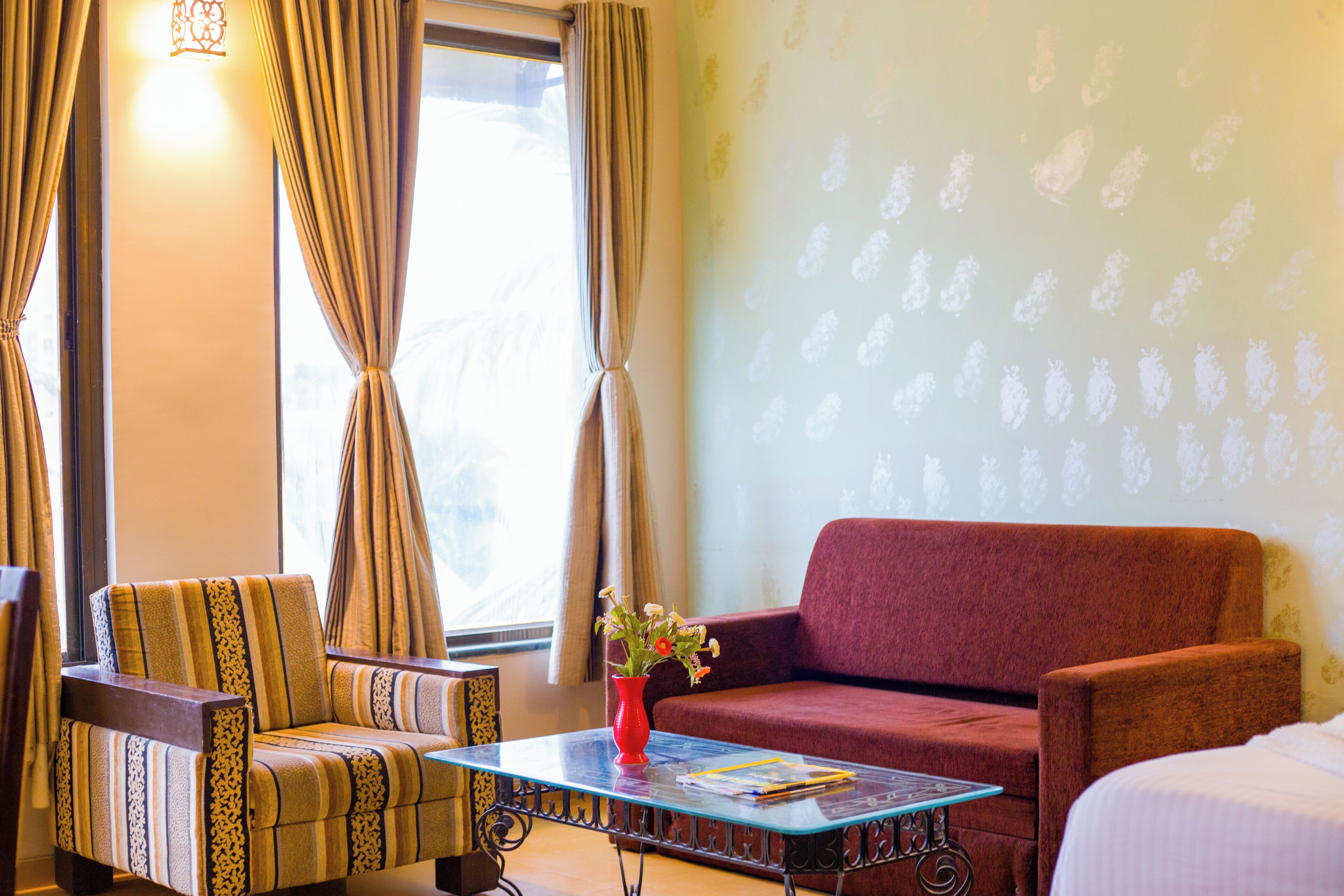 A room with a sofa, armchair, and a small table with a vase of flowers.