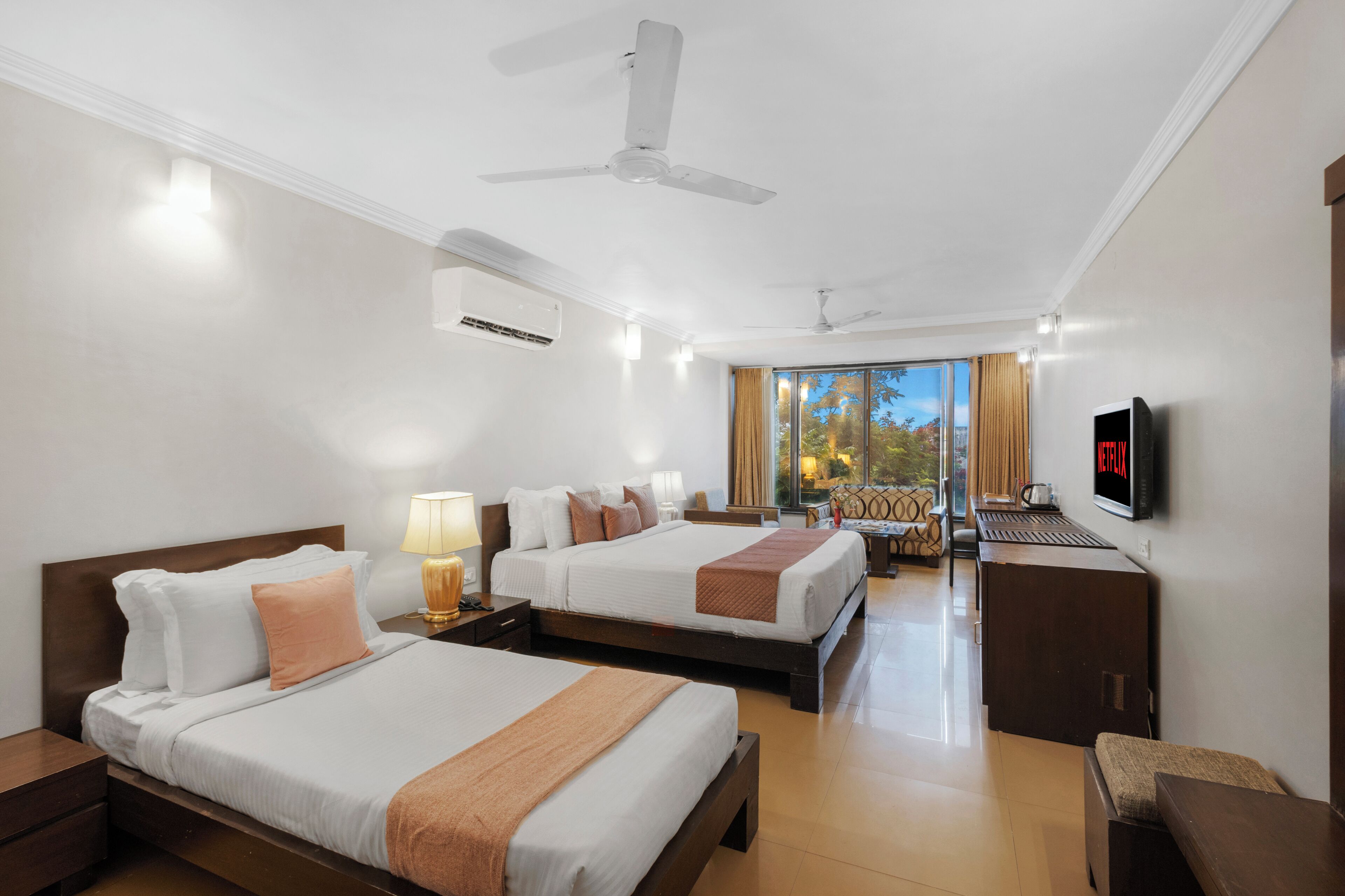 A hotel room with two beds, a TV, a desk, and a large window with a view.