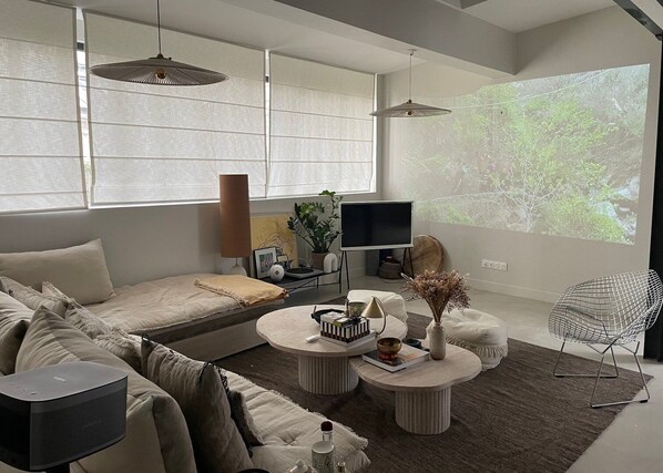 A modern living room with a sofa, two round coffee tables, a TV, and a projector screen displaying a nature scene.