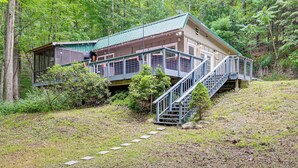 Uma cabana com escadaria de metal que leva a um deck, cercada por uma floresta densa.