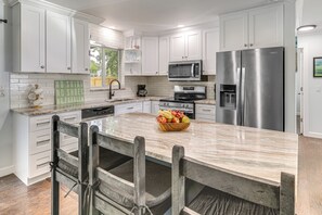 Una cocina moderna con armarios blancos, electrodomésticos de acero inoxidable, encimera de mármol y un frutero.