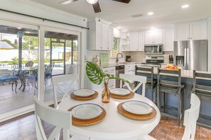A modern kitchen with white cabinets, stainless steel appliances, and a dining area with a white table and chairs. - Swim, Game & BBQ: Family Retreat in Stuart (Stuart)