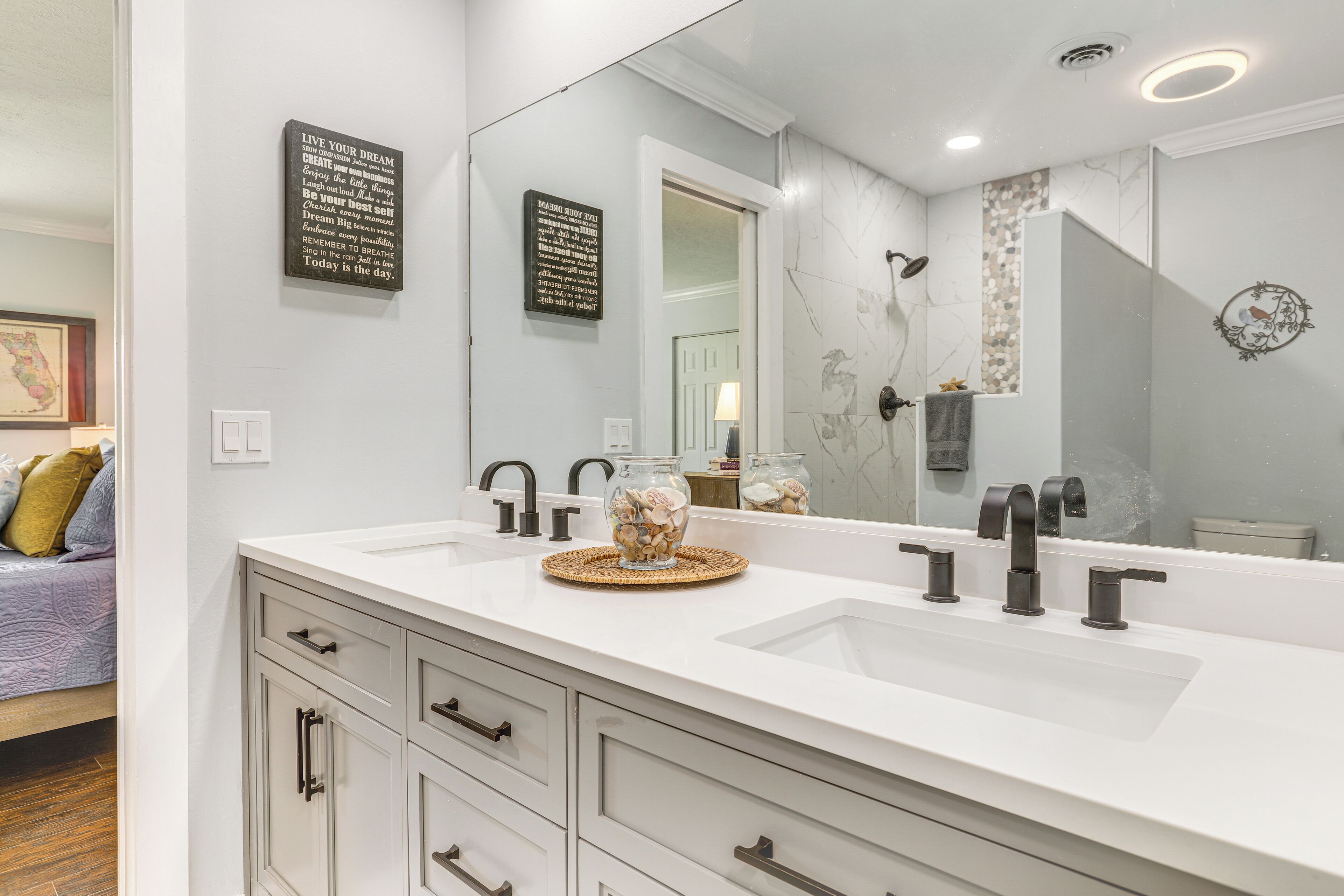 Une salle de bain avec un double lavabo, un grand miroir et un vase décoratif posé sur le comptoir.