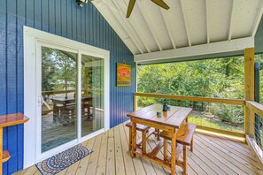 A wooden deck with a table and benches, a glass door leading to an outdoor area, and a view of greenery through the windows. - Lake Hamilton Retreat w/ Kayaks & Spacious Yard! (Hot Springs)