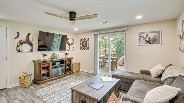 A spacious living room with a wooden coffee table, grey sofas, a large window, and a ceiling fan. - Lake Hamilton Retreat w/ Kayaks & Spacious Yard! (Hot Springs)