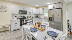 A modern kitchen with white cabinets, a stainless steel refrigerator, and a dining table set with blue plates and glasses. - Lake Hamilton Retreat w/ Kayaks & Spacious Yard! (Hot Springs)