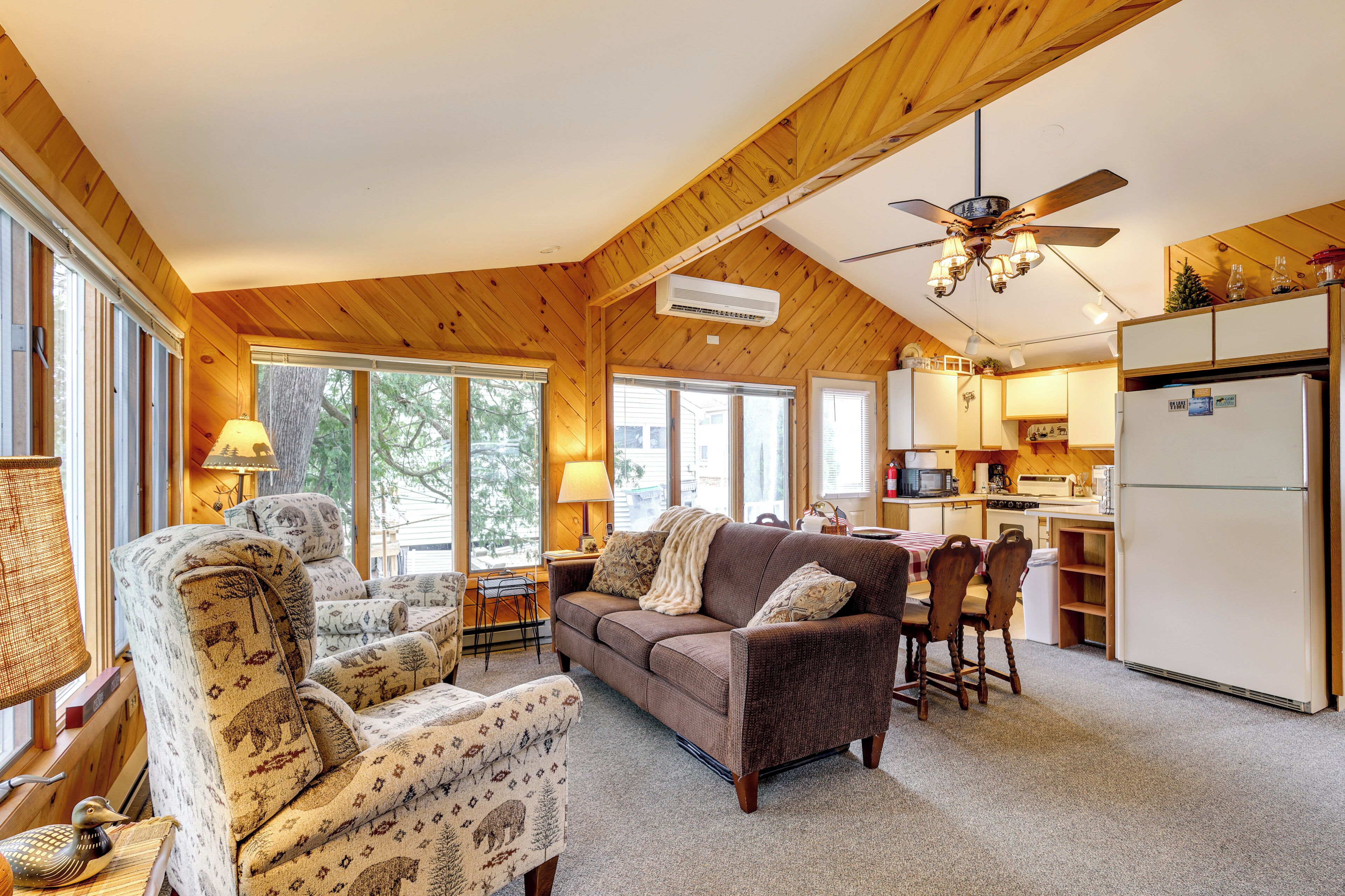 A cozy cabin interior with a wooden ceiling, a sofa, a dining table, and a kitchen area.