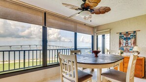 A dining area with a view of the ocean, a ceiling fan, and a wooden table with chairs. - Panoramic Gulf Views: Renovated Fort Myers Condo! (Fort Myers)