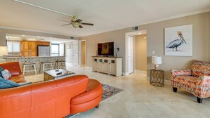 A spacious living room with a modern orange sofa, a patterned armchair, and a flat-screen TV on a wooden cabinet. - Panoramic Gulf Views: Renovated Fort Myers Condo! (Fort Myers)