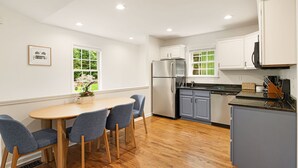 Een moderne keuken met een eethoek, voorzien van een roestvrijstalen koelkast, grijze kastjes en een houten eettafel met blauwe stoelen.