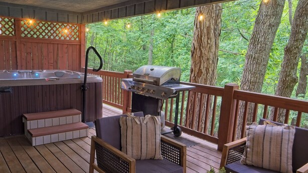 Een houten terras met een hottub, barbecue, zithoek en sfeerverlichting.
