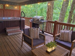 Una terraza de madera con jacuzzi, parrilla, zona de estar y luces colgantes.