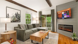 A modern living room with a sectional sofa, a wooden coffee table, a fireplace, and a flat-screen TV displaying streaming services.