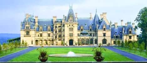 A large, historic building with a symmetrical facade, a central entrance, and a well-maintained lawn with a fountain.