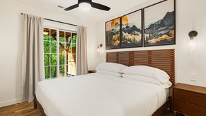 A bedroom with a bed, wooden headboard, and a large window with curtains.