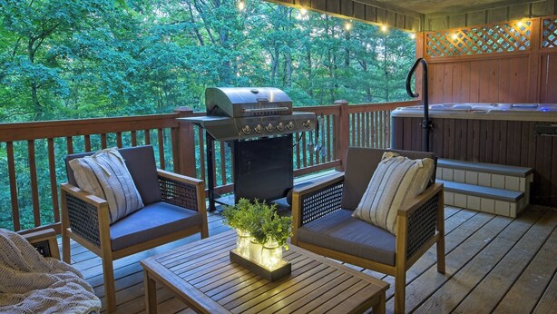 A deck with wooden furniture, a grill, and a hot tub.