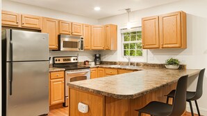 A kitchen with wooden cabinets, stainless steel appliances, a granite countertop, and a window with a view of greenery.