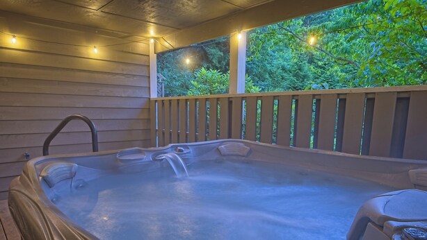 A hot tub with a wooden deck and a view of greenery. - Hot Tub · Fire Pit · EV Charger · Near Asheville (Asheville)