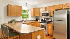 A modern kitchen with wooden cabinets, granite countertops, stainless steel appliances, and a window with a view of greenery. - Hot Tub · Fire Pit · EV Charger · Near Asheville (Asheville)