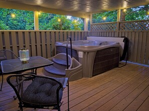 Een overdekt terras buiten met een hottub, een tafel en stoelen.