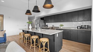 Une cuisine moderne avec des meubles de couleur sombre, un plan de travail en granit et trois tabourets en bois.