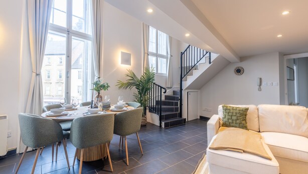 Ein modernes Wohnzimmer mit Essbereich, Treppe und einer Couch.