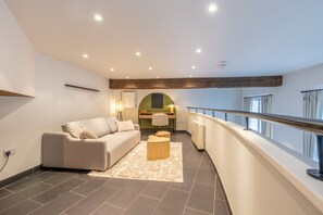A modern living room with a sofa, a coffee table, and a desk with a chair. There is a balcony with a railing and a view of the outside. - Watergate in Newcastle Upon Tyne (Newcastle-upon-Tyne)