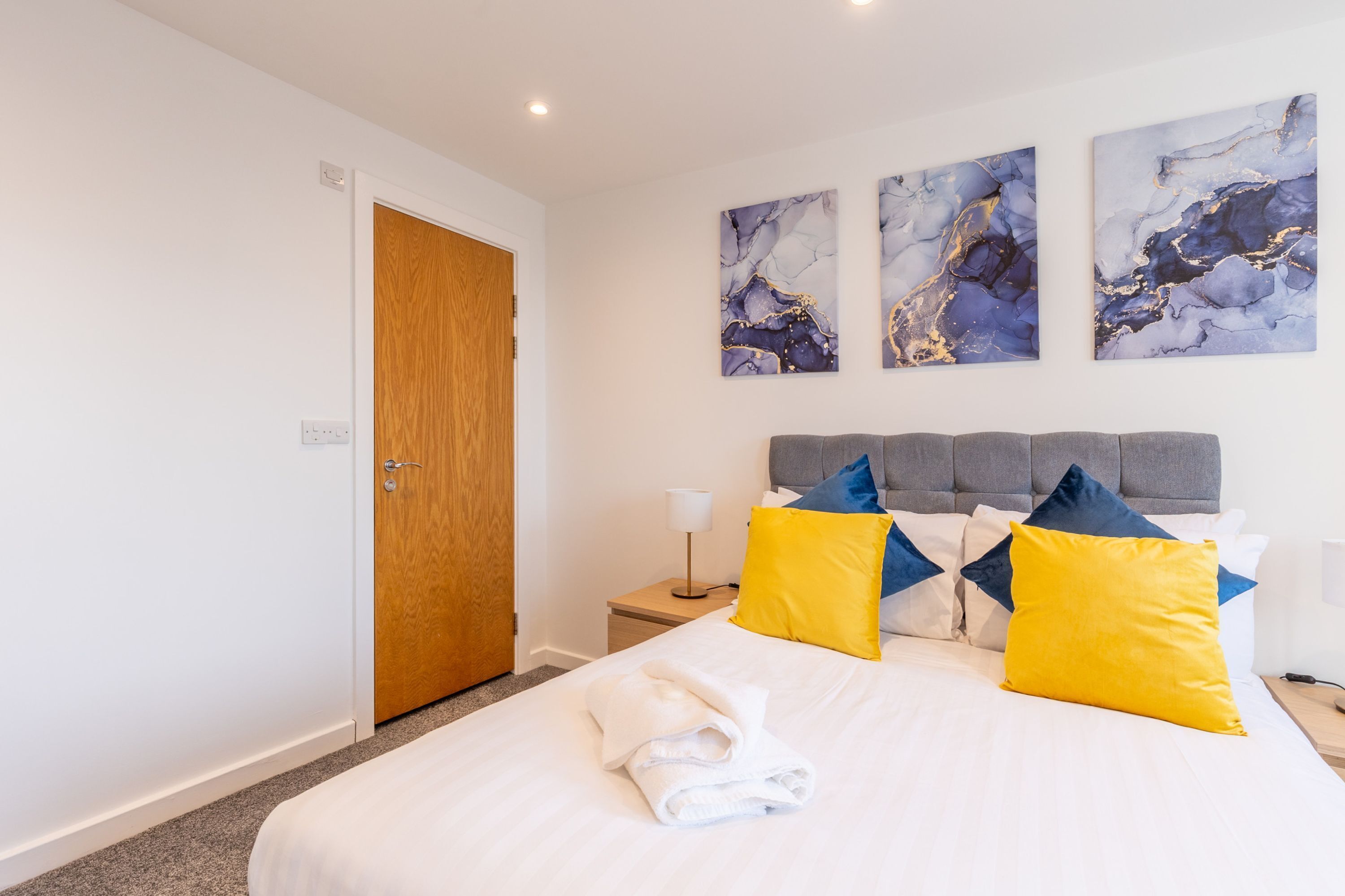 A hotel room with a bed, a wooden door, and marble artwork on the wall.