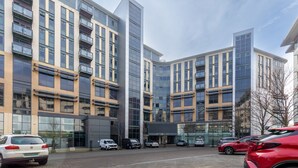 Un bâtiment moderne à plusieurs étages, doté de grandes fenêtres et d’un parking où sont stationnées différentes voitures.