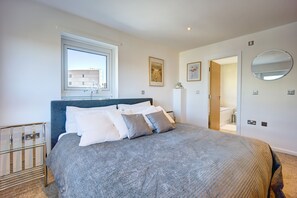 A modern bedroom with a large bed, a bedside table, a window, and a bathroom visible through an open door. - Atico in Newcastle Upon Tyne (Newcastle-upon-Tyne)