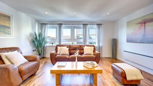 A living room with a brown leather sofa, a wooden coffee table, and a large window with curtains. - Atico in Newcastle Upon Tyne (Newcastle-upon-Tyne)