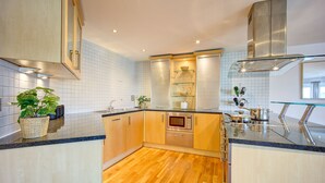 A modern kitchen with wooden cabinets, a stainless steel microwave, and a glass backsplash. - Atico in Newcastle Upon Tyne (Newcastle-upon-Tyne)