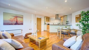 A modern living room with a wooden floor, leather sofas, a coffee table, and a dining area with a glass table and chairs. - Atico in Newcastle Upon Tyne (Newcastle-upon-Tyne)