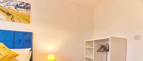 A bedroom with a bed, bedside table with a lamp, a wardrobe, and a painting on the wall.