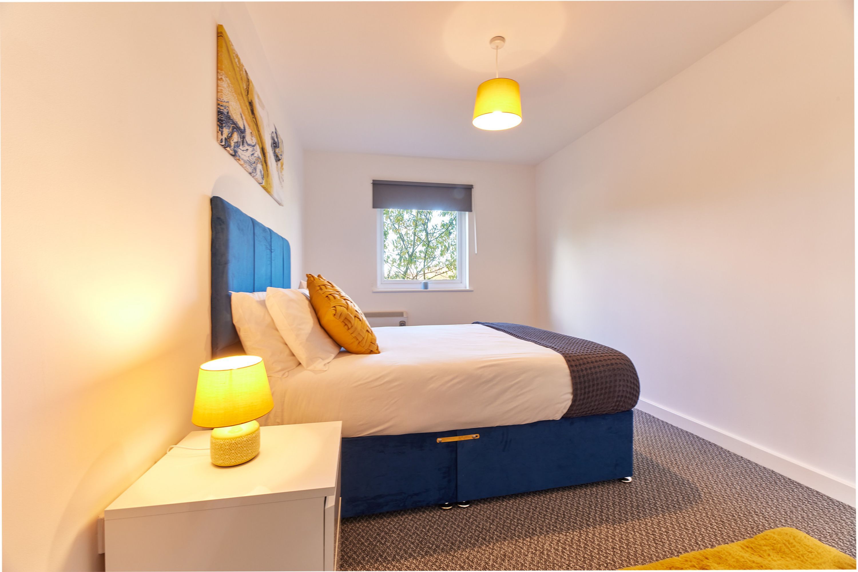 Een slaapkamer met een bed, nachtkastje, lamp en raam.