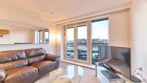 A modern living room with a leather sofa, a glass coffee table, a flat-screen TV, and large windows offering a city view. - Thornton in Newcastle Upon Tyne (Newcastle-upon-Tyne)