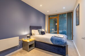 A bedroom with a large bed, a nightstand, a window with blinds, and a view of the outdoors. - The Close in Newcastle Upon Tyne (Newcastle-upon-Tyne)