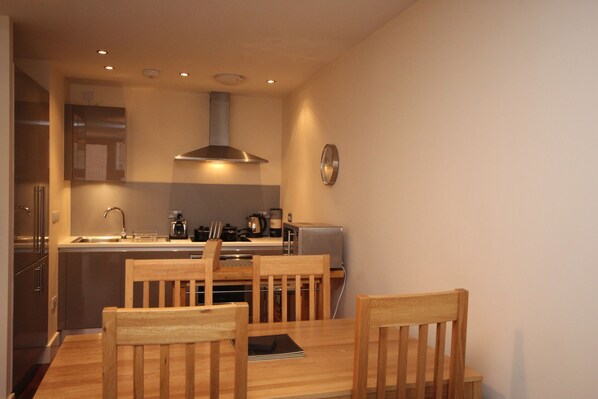 A compact kitchen with modern appliances, wooden dining table, and chairs. - Fir in Newcastle Upon Tyne (Newcastle-upon-Tyne)
