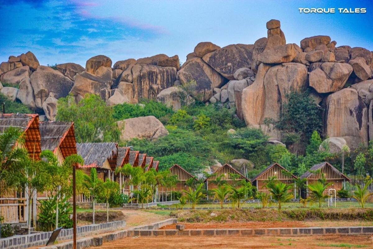 A resort with thatched-roof huts, a rocky backdrop, and lush greenery.