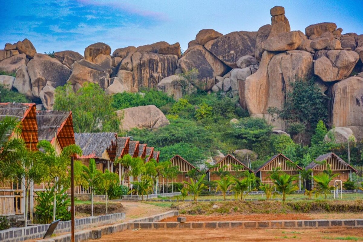 Ein Resort mit strohgedeckten Hütten, einem felsigen Hintergrund und üppiger Vegetation.