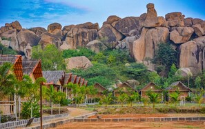 Ein Resort mit strohgedeckten Hütten, einem felsigen Hintergrund und üppiger Vegetation.