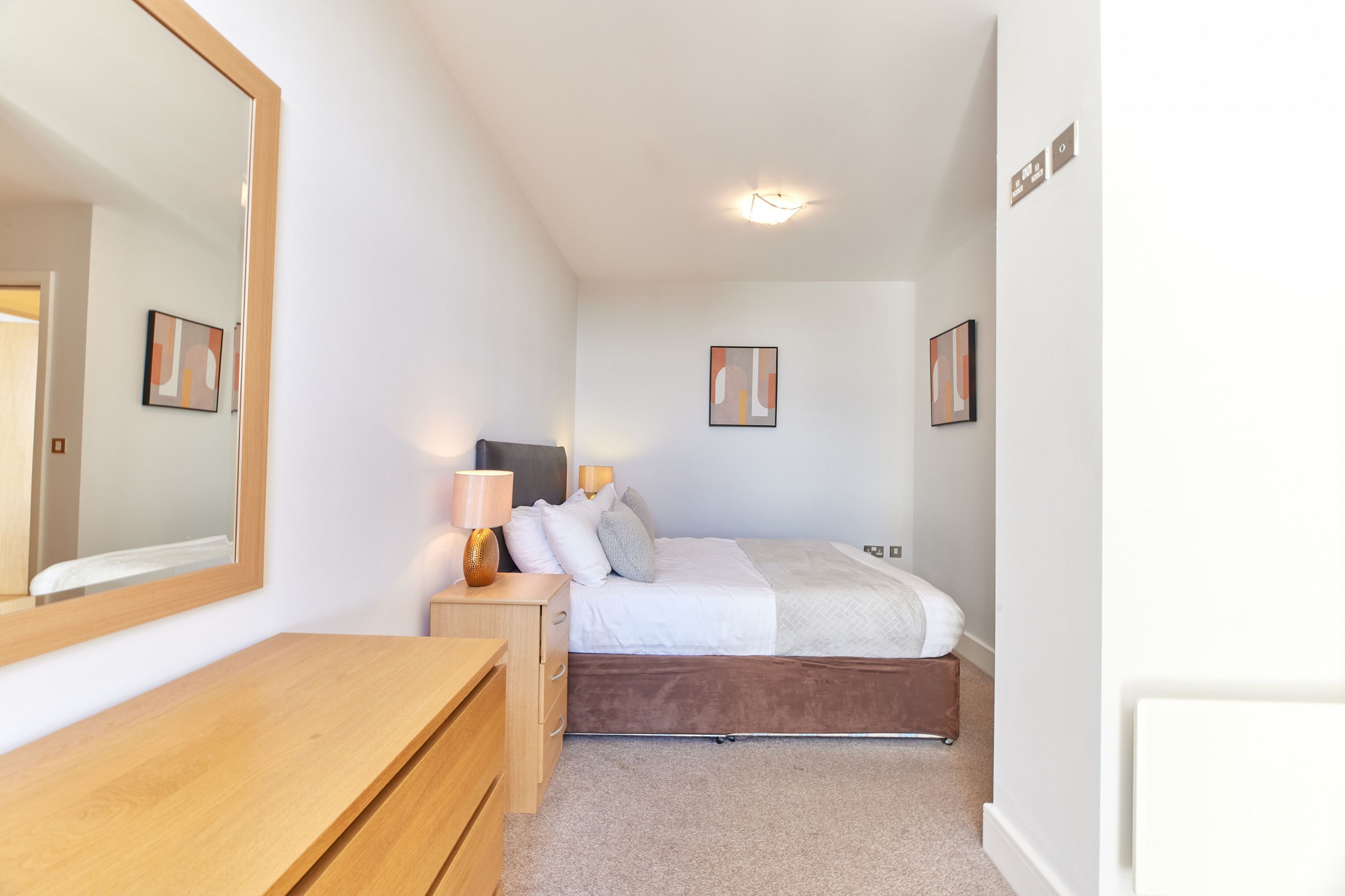 A bedroom with a bed, bedside table, lamp, and a large mirror.