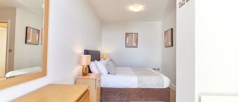 A bedroom with a bed, bedside table, lamp, and a large mirror.