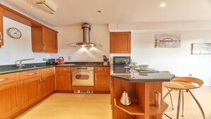 A modern kitchen with wooden cabinets, stainless steel appliances, and a central island with bar stools. - The Peak in Newcastle Upon Tyne (Newcastle-upon-Tyne)