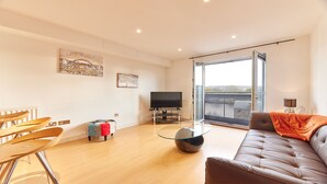 A modern living room with a sofa, a glass coffee table, a TV, and a view of a river through a large window. - The Peak in Newcastle Upon Tyne (Newcastle-upon-Tyne)