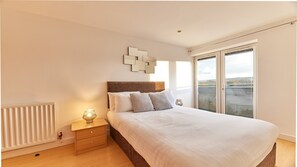 A bedroom with a large bed, a nightstand, a wall-mounted light, and a view of the outdoors through a sliding glass door. - The Peak in Newcastle Upon Tyne (Newcastle-upon-Tyne)
