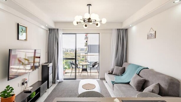 Ein modernes Wohnzimmer mit Sofa, Fernseher, Deckenleuchte und einem Balkon mit Blick.