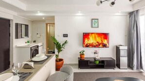 Ein modernes Wohnzimmer mit Flachbildfernseher, einer Couch, einem Esstisch mit Stühlen, einer Küchenzeile und einer Zimmerpflanze.