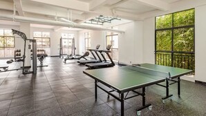 Ein geräumiger Fitnessraum mit Trainingsgeräten, einem Tischtennis-Tisch und großen Fenstern mit Blick auf Grünflächen.